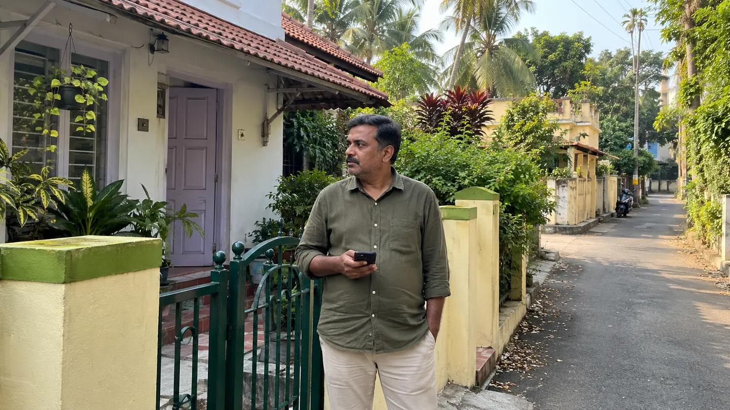 A recipient waits by a green pedestrian gate on a Mysuru residential lane