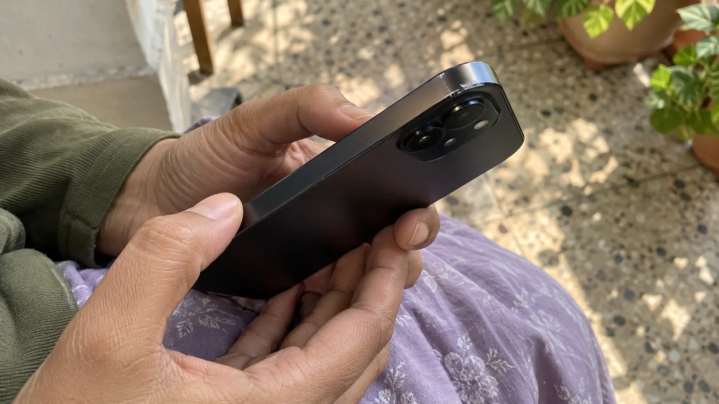 Hands show the scuffed corner and rear camera area of an older phone before resale